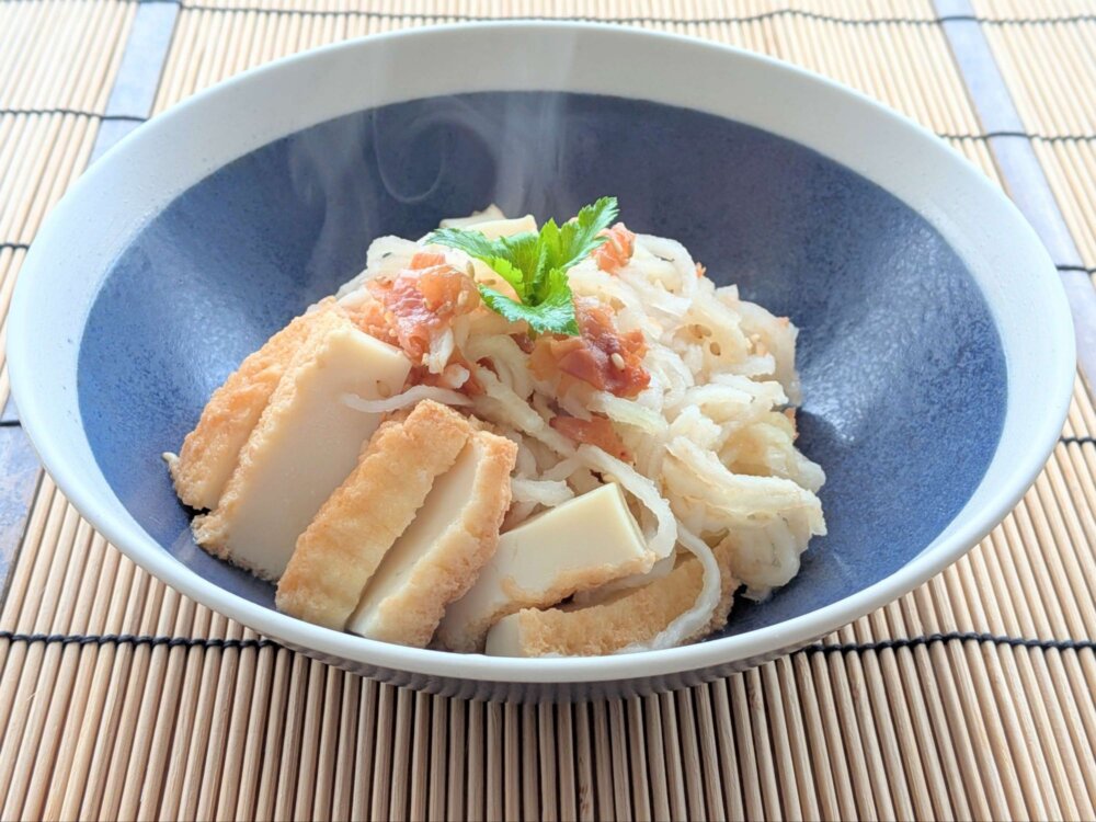 青い器に盛り付けた切り干し大根と厚揚げの煮物。上には砕いた梅干しと三つ葉がのせられている様子